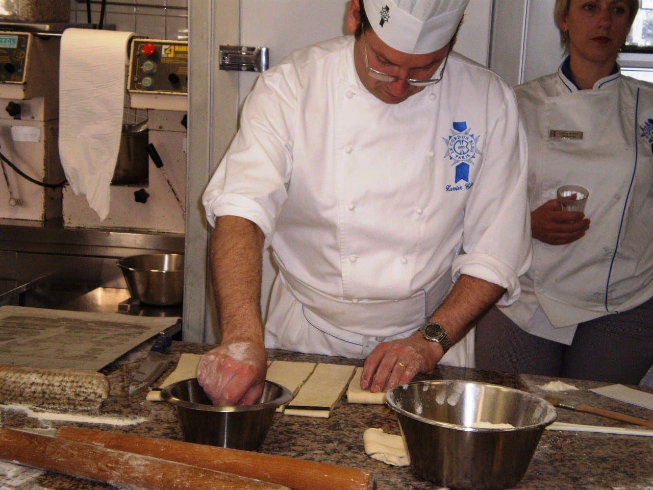 Chef in Le Cordon Bleu whites working pastry dough at a teaching kitchen bench during a pastry class