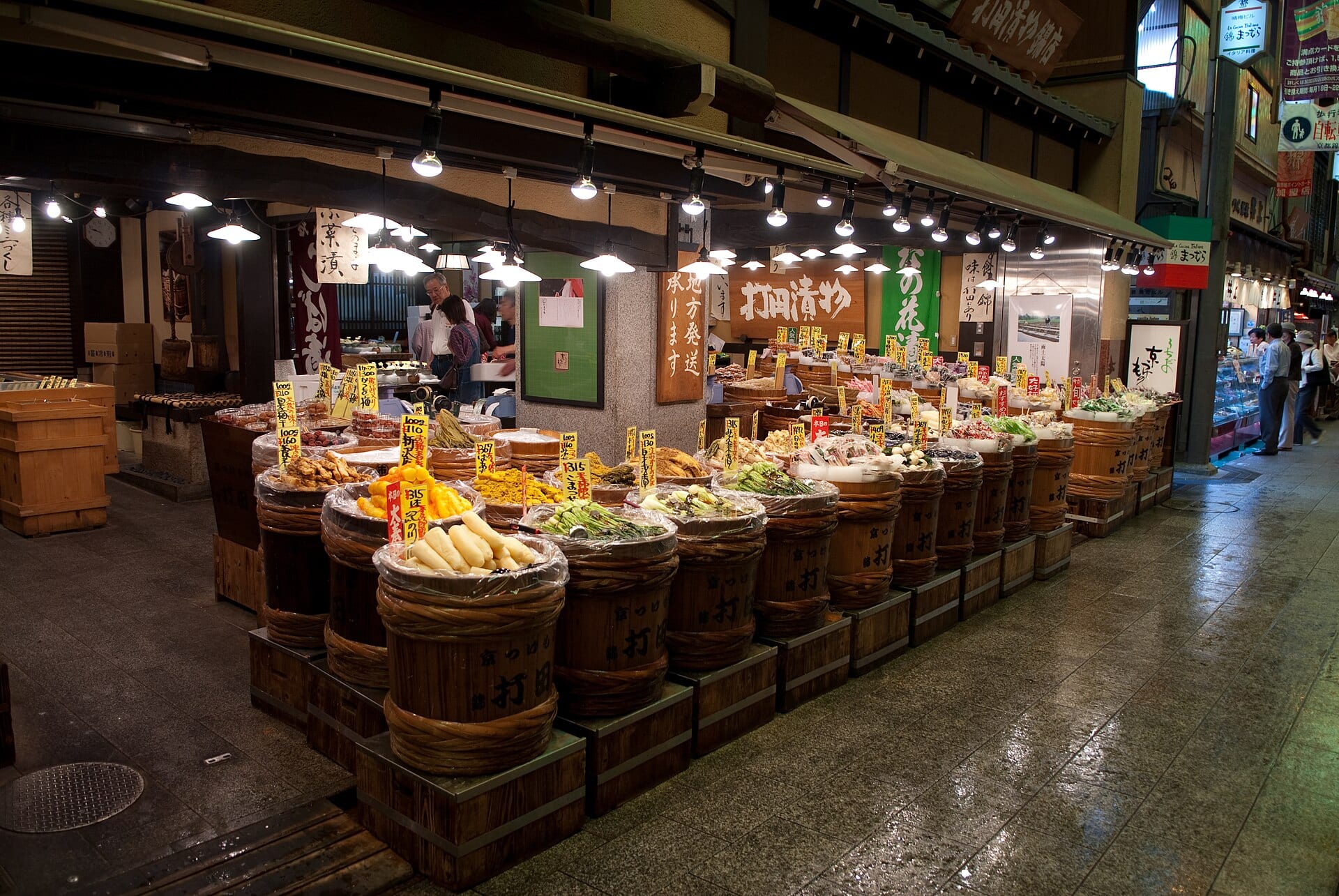 A pickle shop in Kyoto's Nishiki Market with wooden barrels of tsukemono and price tags under warm lights